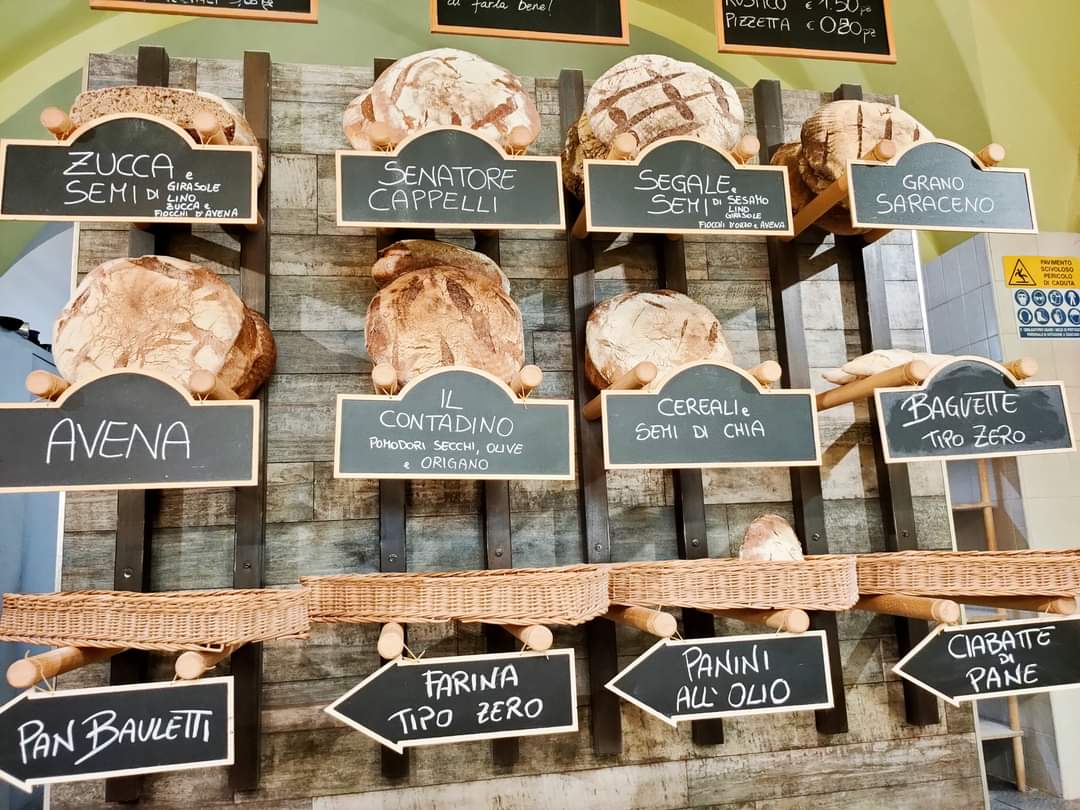 Breads and baked goods arranged on bakery shelves with handwritten product labels